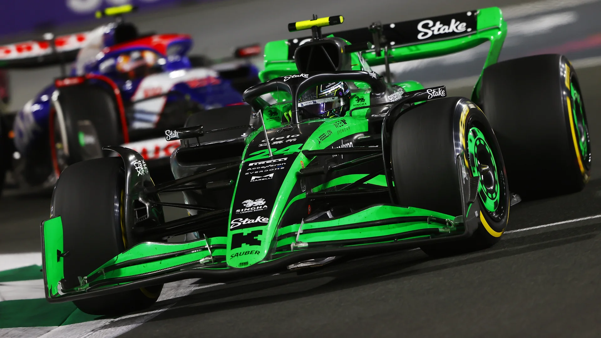 A green and black Formula 1 car racing on the track at the 2024 Saudi Arabian Grand Prix under bright lights, with another car closely behind.