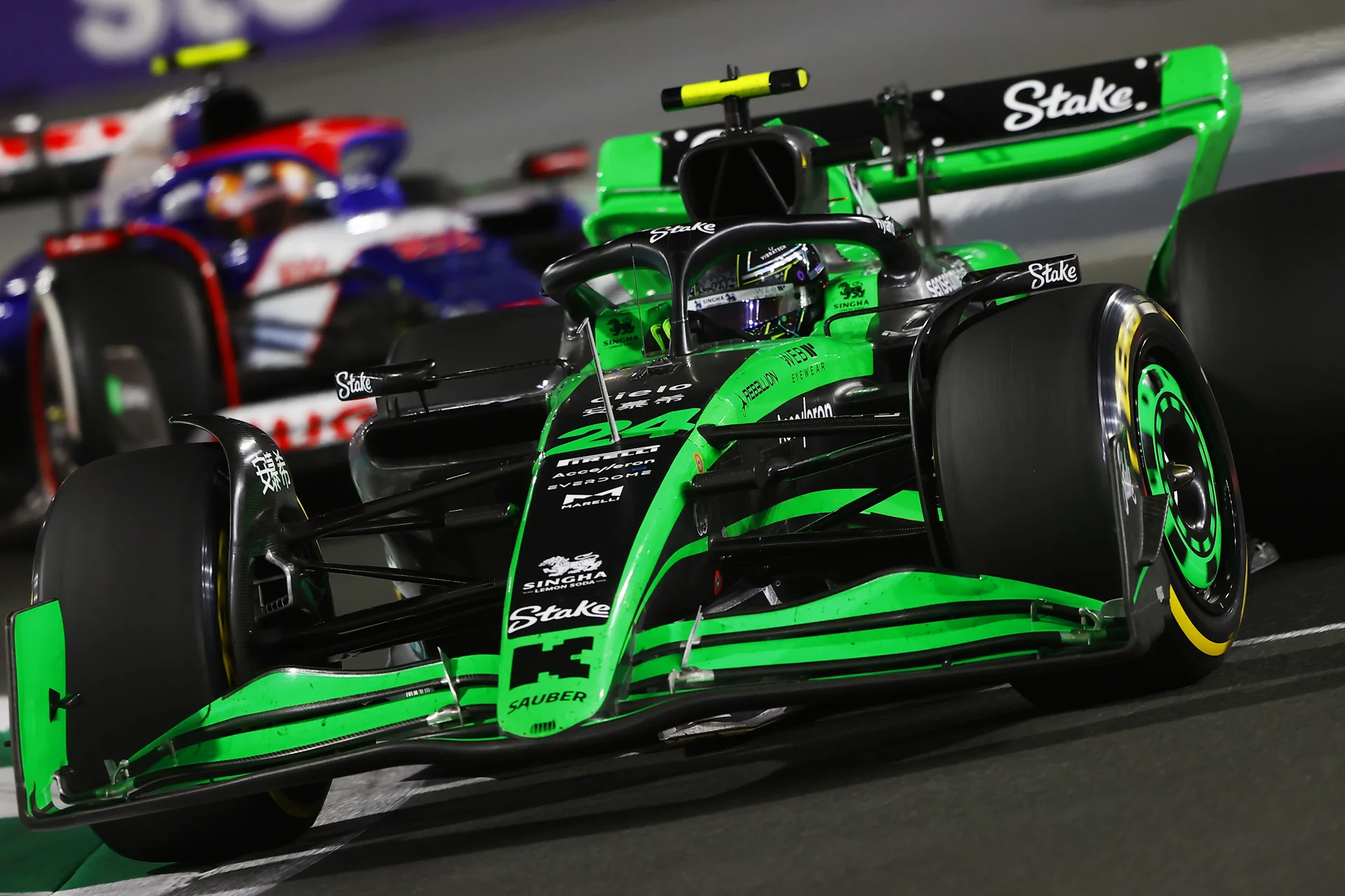 A green and black Formula 1 car racing on the track at the 2024 Saudi Arabian Grand Prix under bright lights, with another car closely behind.