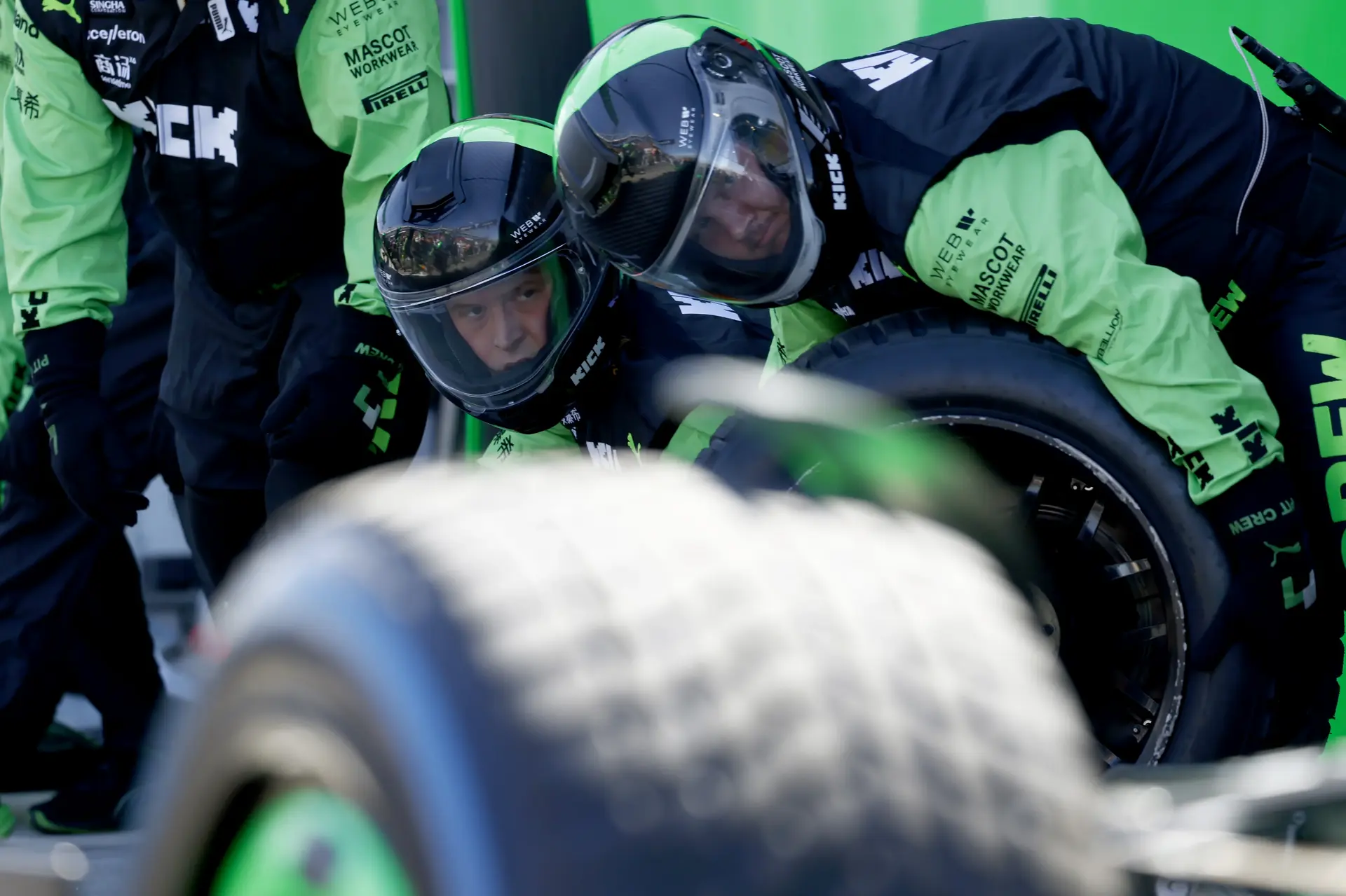 Mechanics in green uniforms working on the body of a Formula 1 car, focusing on composite material adjustments in the garage.