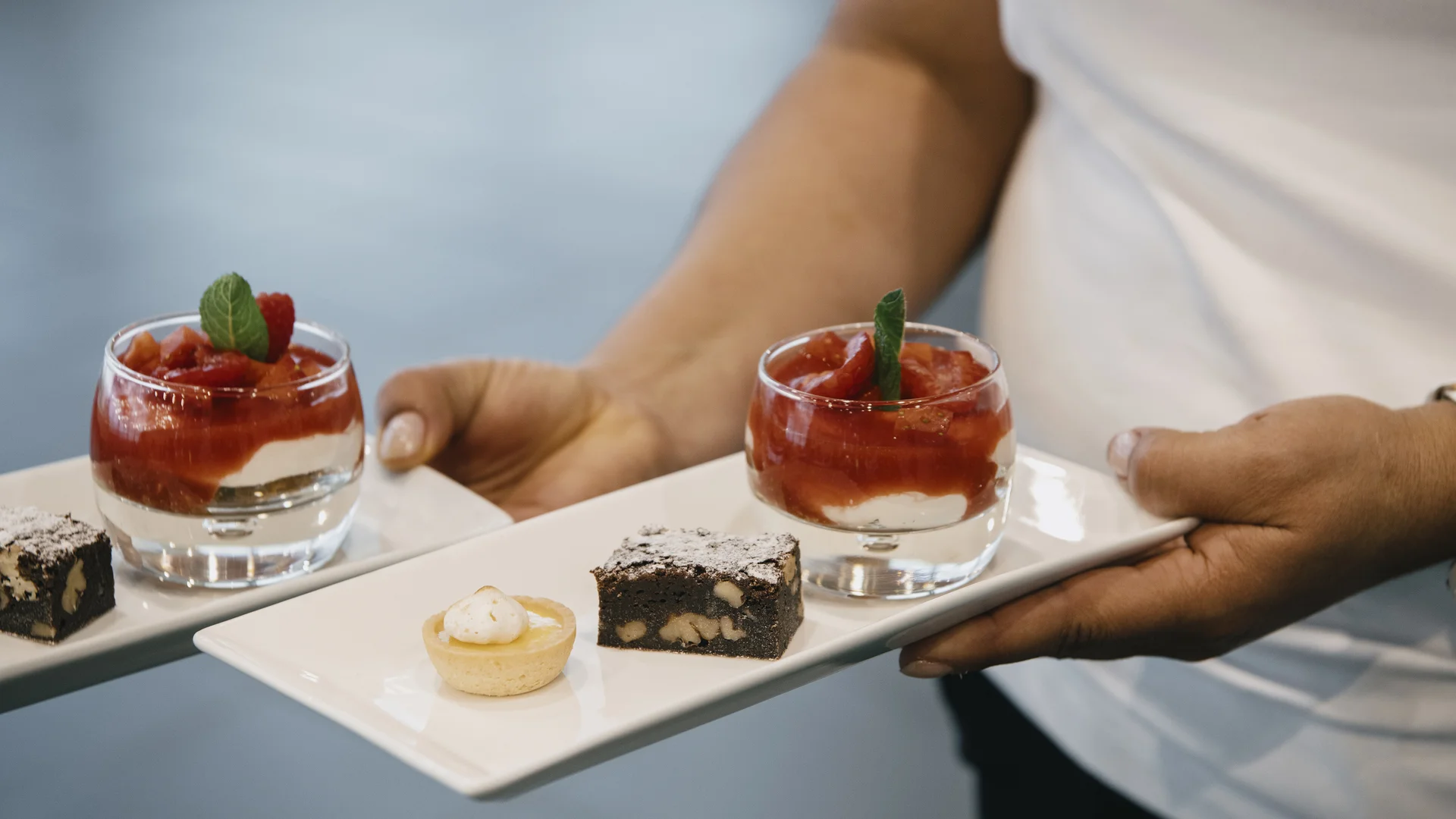 A server presenting a tray of elegant desserts, including fruit-topped pastries and chocolate treats, at a premium event in Hinwil.