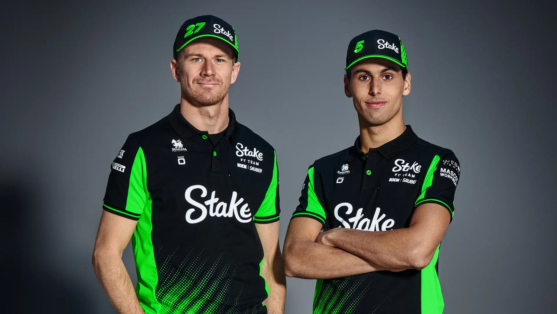 F1 drivers Nico Hülkenberg and Gabriel Bortoleto posing in the Sauber F1 Team's 2025 Code-Zero teamwear, featuring a black and green gradient design with Stake branding, standing side by side with their arms crossed.