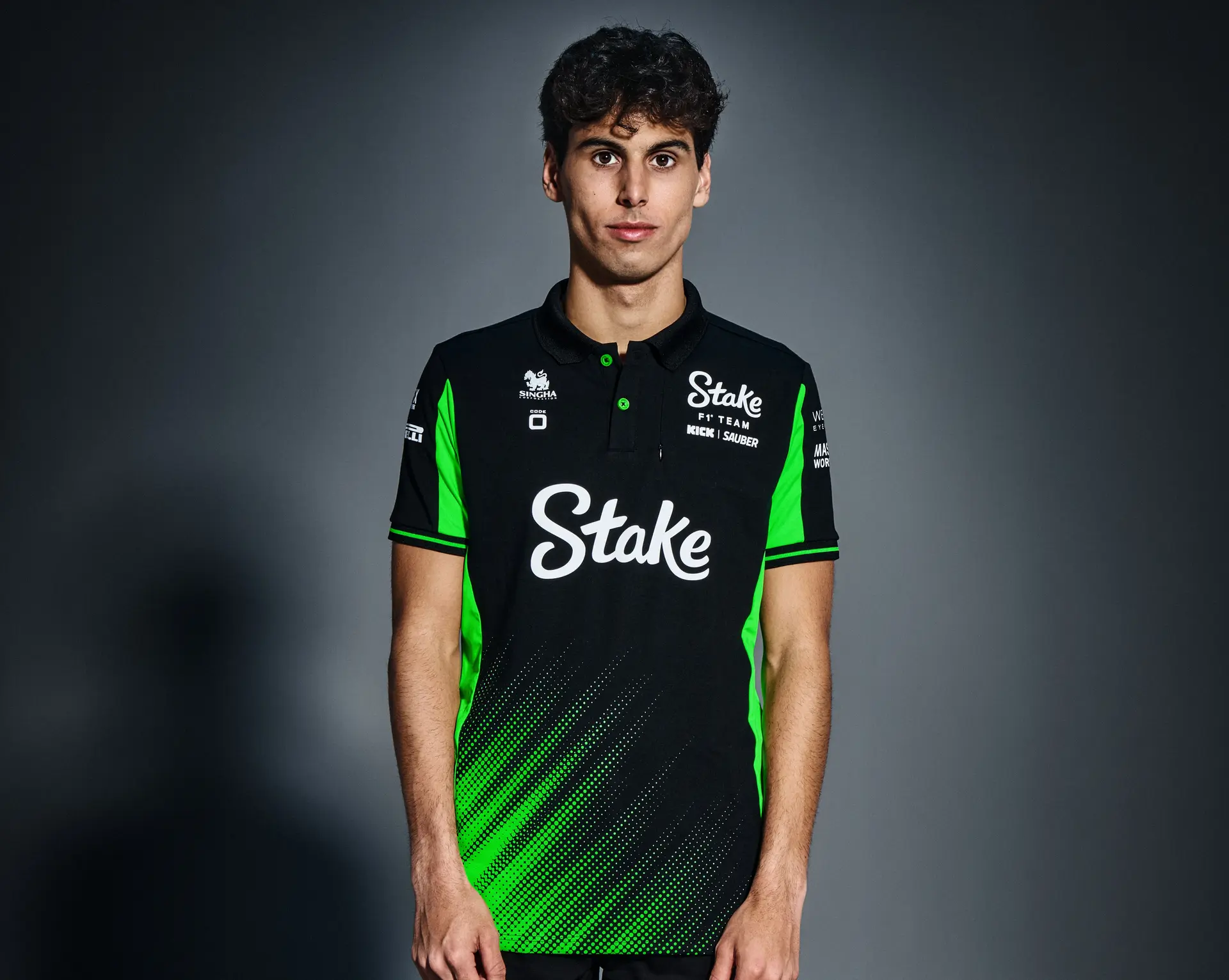 Portrait of F1 driver Gabriel Bortoleto wearing the Sauber F1 Team's 2025 teamwear, featuring a black and green design with Stake sponsorship branding.