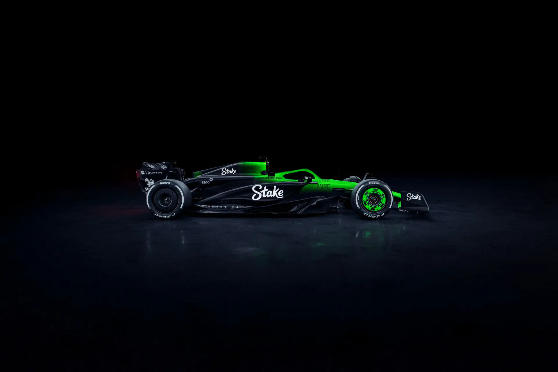 Side profile of the Sauber C45 Formula 1 car, featuring the Stake sponsorship and an illuminated green and black livery against a dark background. The aerodynamic shape and sleek bodywork are accentuated by the lighting, showcasing the sidepod design and rear wing.