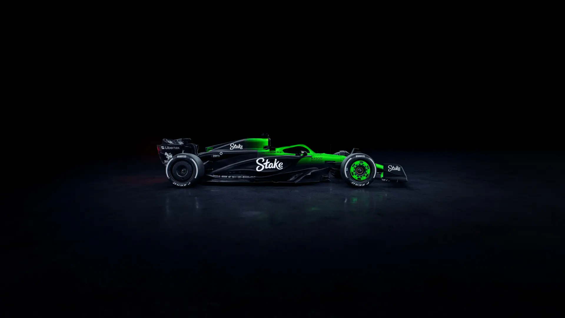 Side profile of the Sauber C45 Formula 1 car, featuring the Stake sponsorship and an illuminated green and black livery against a dark background. The aerodynamic shape and sleek bodywork are accentuated by the lighting, showcasing the sidepod design and rear wing.