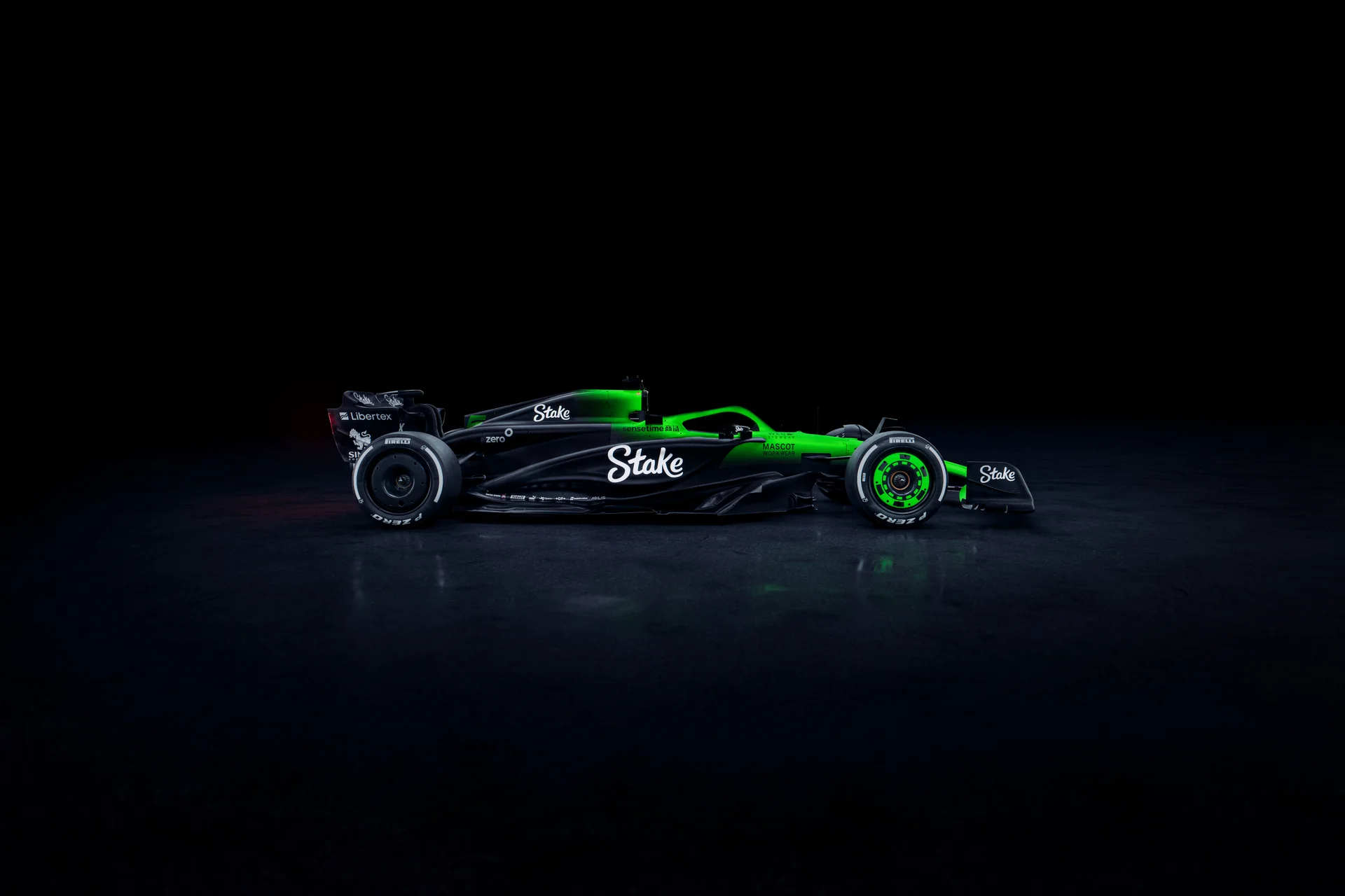 Side profile of the Sauber C45 Formula 1 car, featuring the Stake sponsorship and an illuminated green and black livery against a dark background. The aerodynamic shape and sleek bodywork are accentuated by the lighting, showcasing the sidepod design and rear wing.