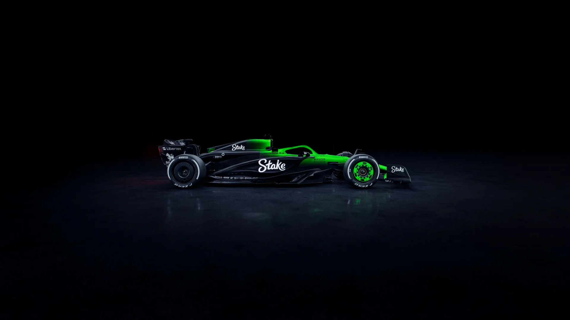 Side profile of the Sauber C45 Formula 1 car, featuring the Stake sponsorship and an illuminated green and black livery against a dark background. The aerodynamic shape and sleek bodywork are accentuated by the lighting, showcasing the sidepod design and rear wing.