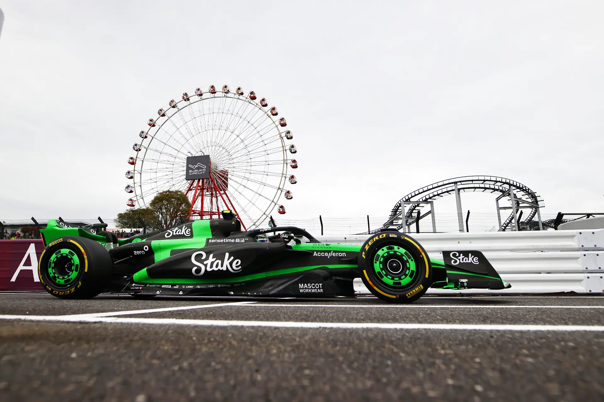A green and black Formula 1 car on track during the 2024 Japanese Grand Prix Friday practice session, with the iconic Suzuka Circuit Ferris wheel in the background.