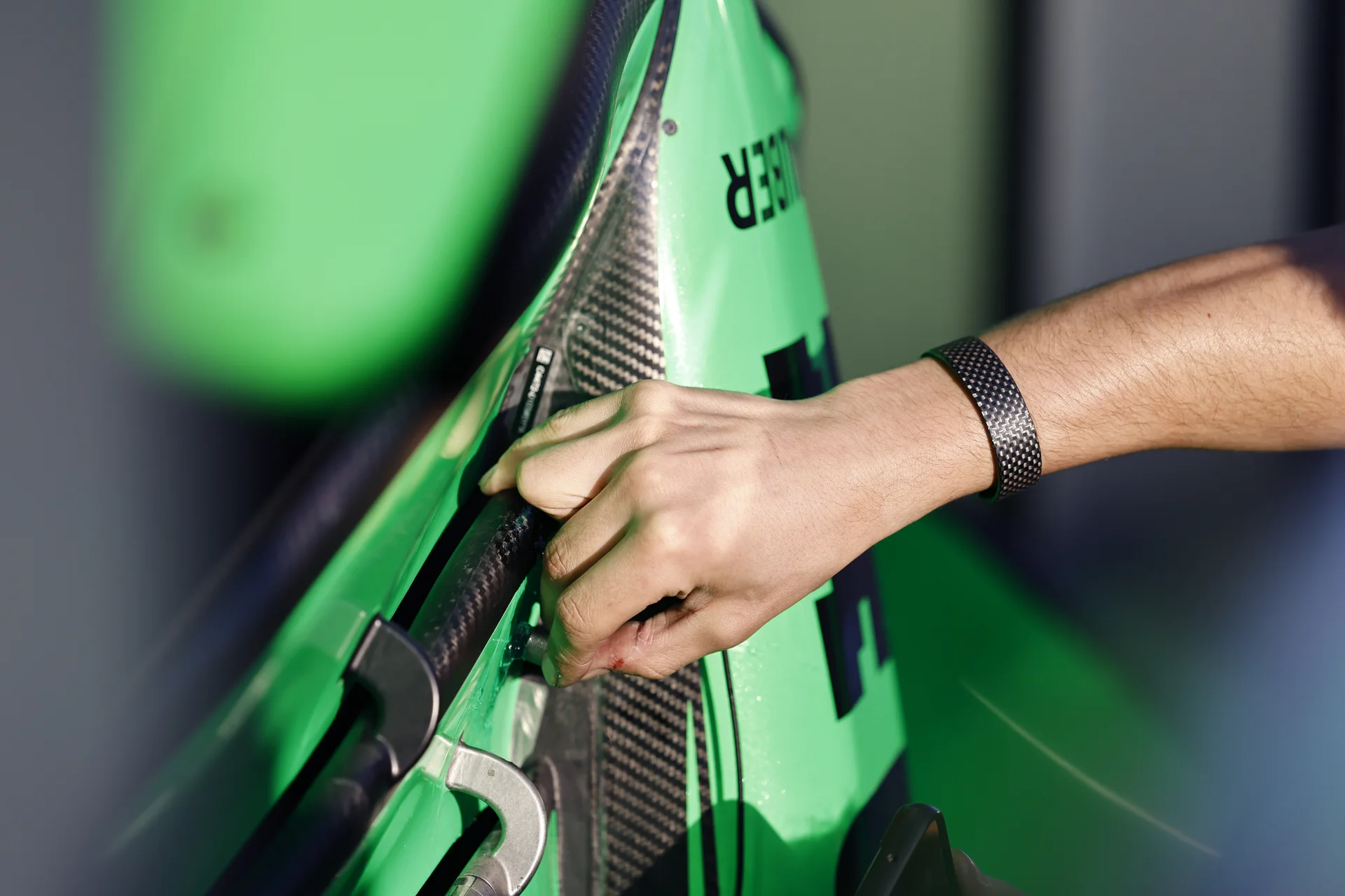A close-up of a technician's hands fitting or adjusting a green carbon fiber component on a Formula 1 car.