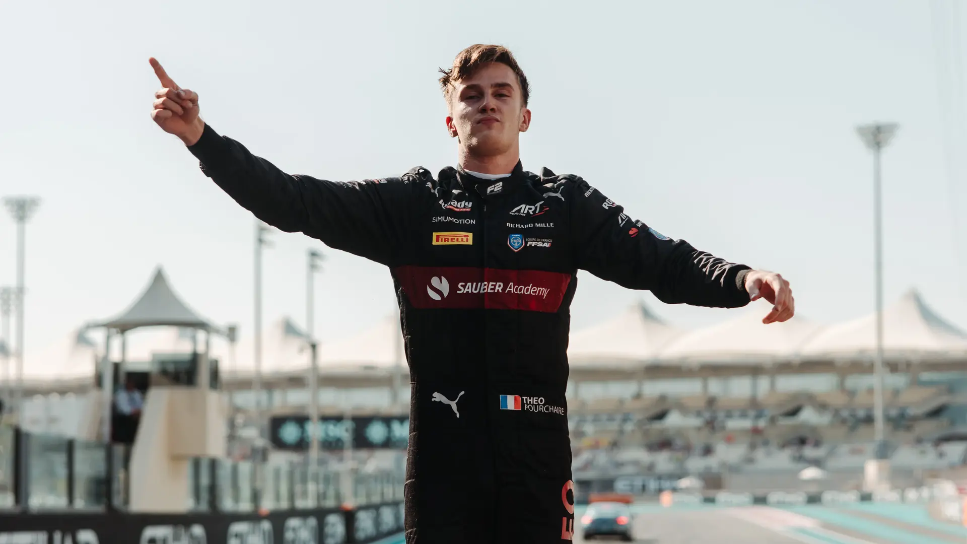 A Sauber Formula 1 driver celebrating on top of their car at the 2023 Abu Dhabi Grand Prix, raising their arms in victory with the racetrack in the background.