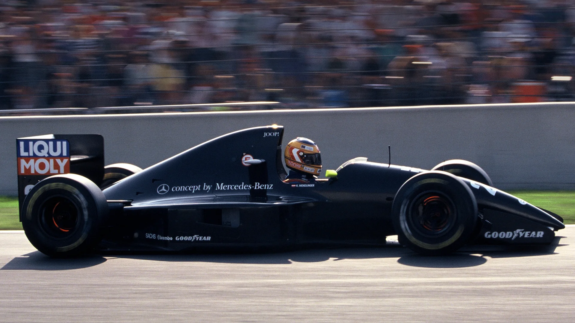 A historic Sauber Formula 1 car racing on track, captured in motion with a blurred background of spectators.