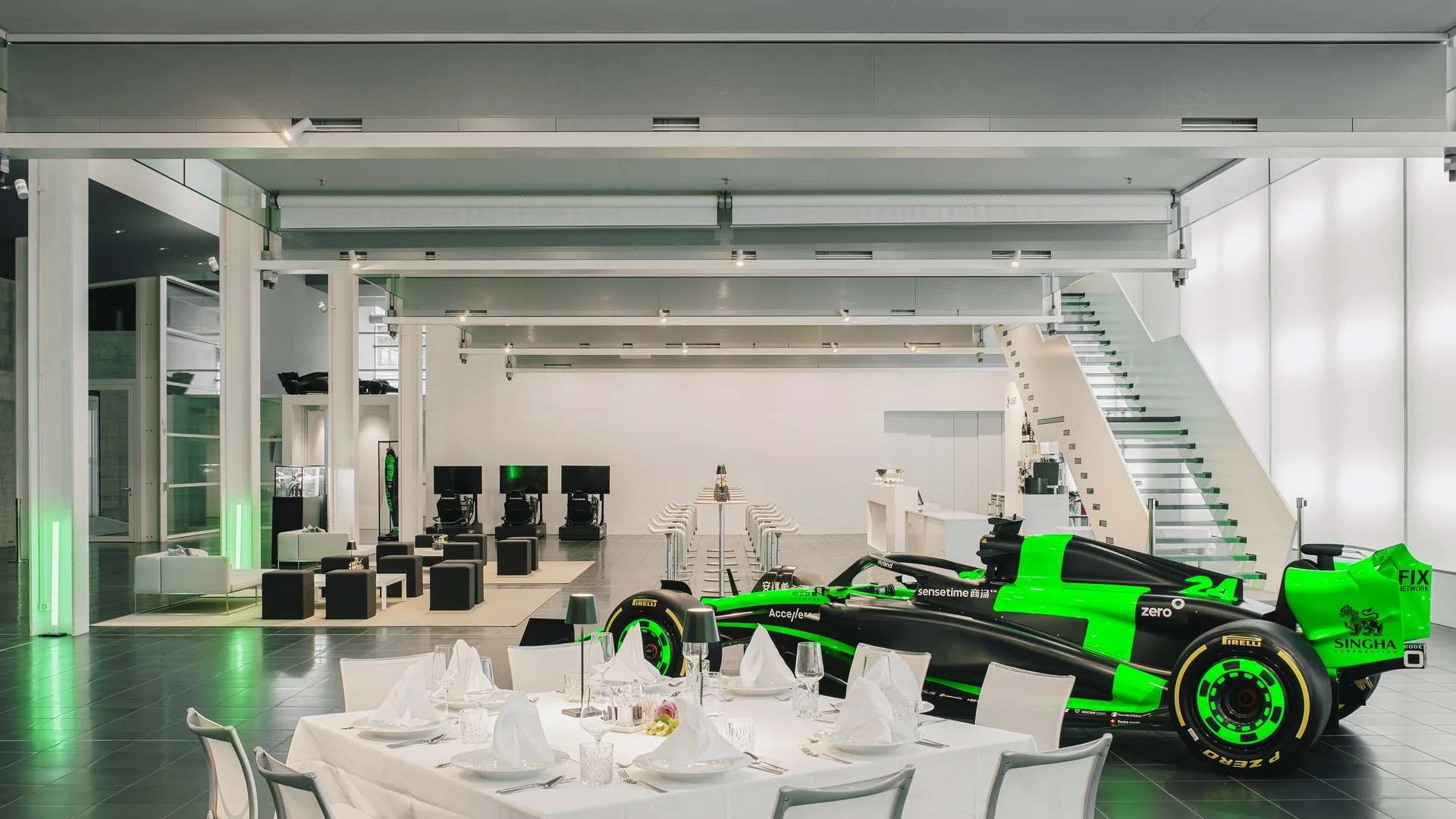 Elegant event setup in a modern venue, featuring white-clothed tables and green-lit racing simulators in the background.
