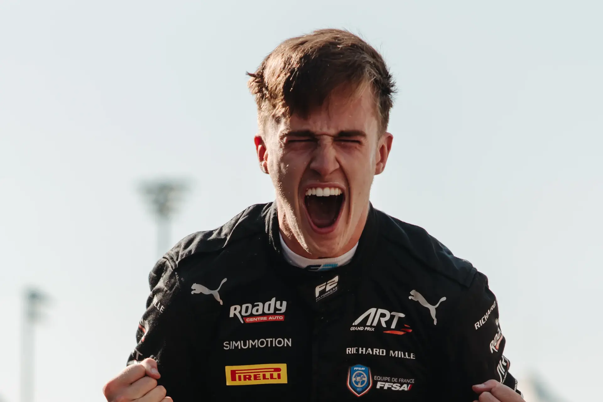 Theo Pourchaire celebrating at the 2023 Abu Dhabi Grand Prix, clenching his fists and smiling triumphantly while wearing his Sauber racing suit.