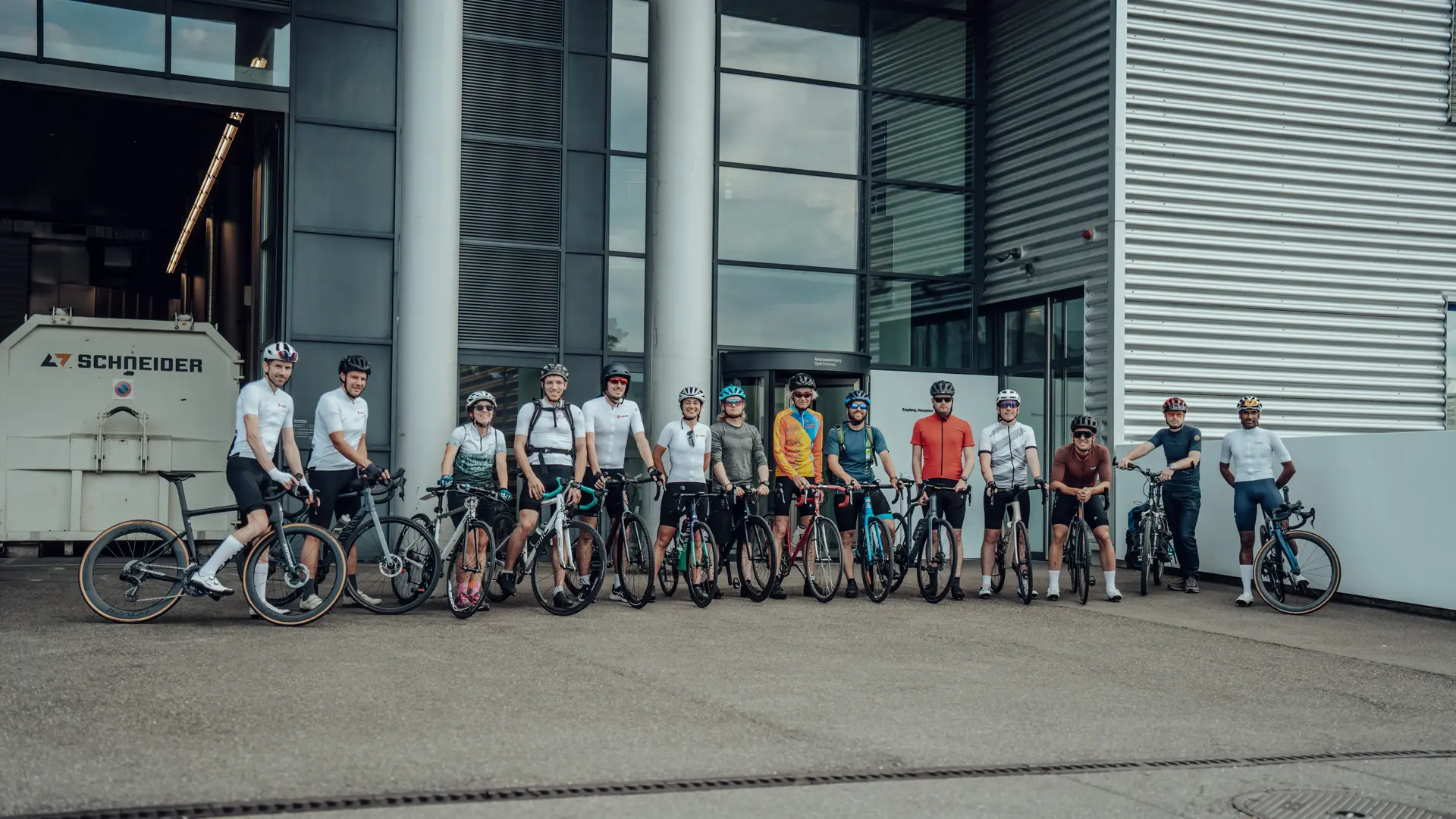Group of Sauber Motorsport employees and cycling enthusiasts gathered for an industrial building for an afterwork cycling event.