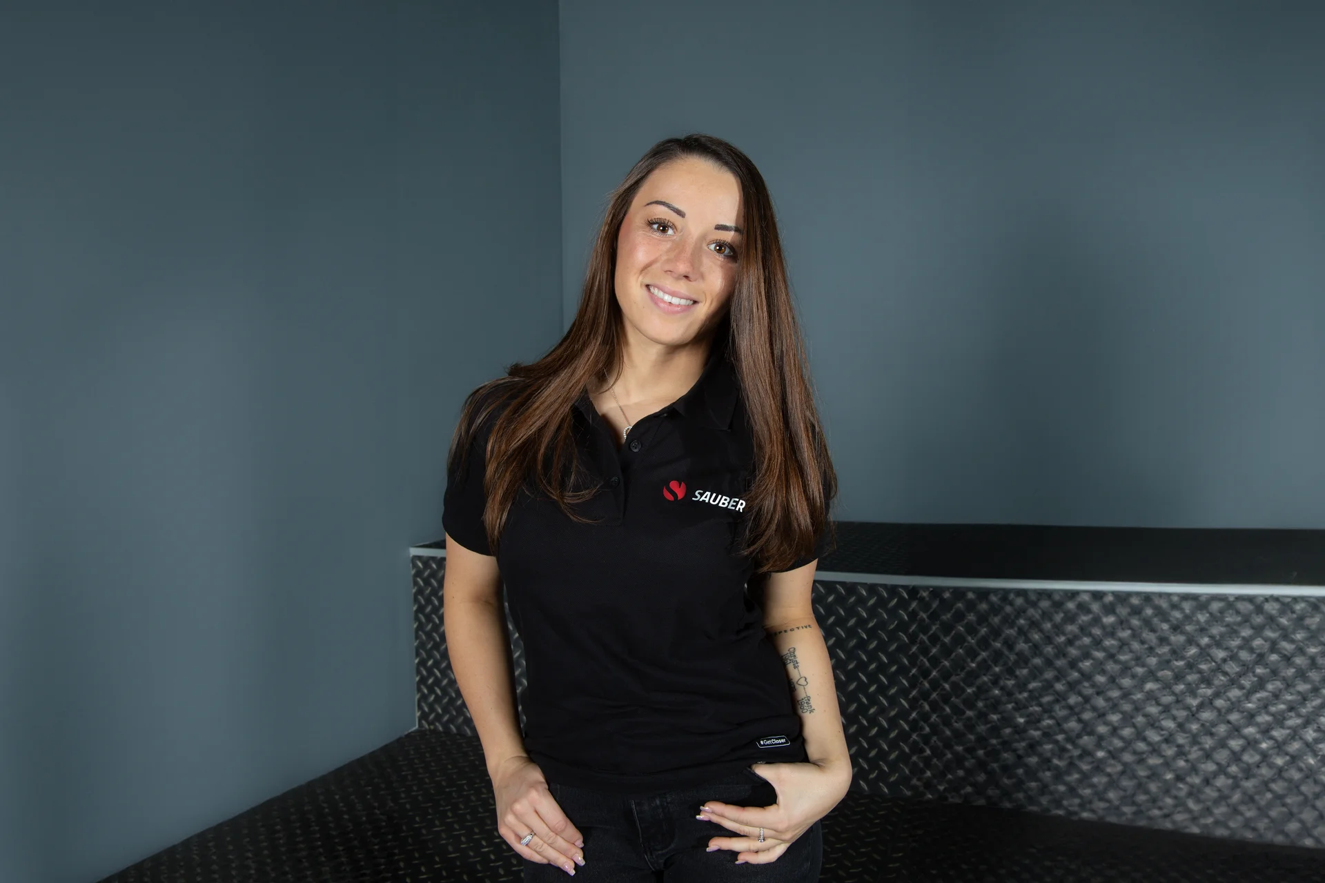 Carrie Schreiner, F1 Academy driver for Sauber, sitting on a couch in team apparel, looking confident.