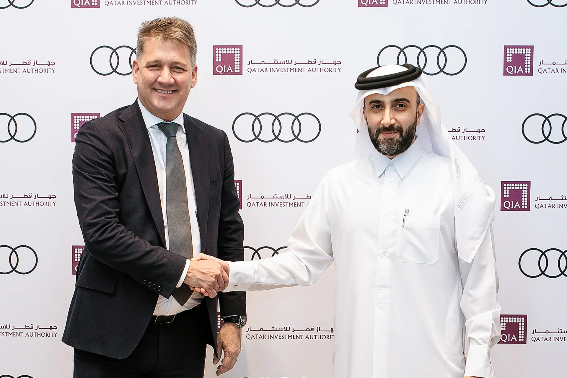 Two executives shaking hands during a partnership signing ceremony for the Sauber F1 Team, with a branded backdrop displaying logos of sponsors and event partners.