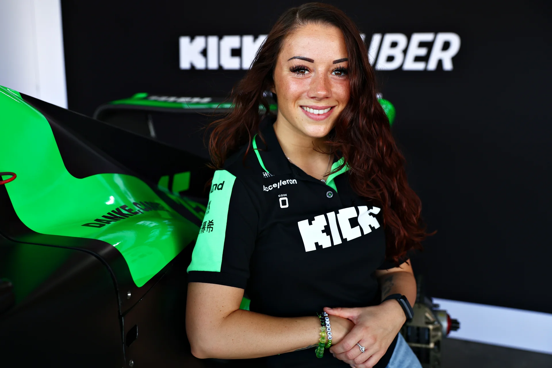 Carrie Schreiner, professional racing driver, announced as the new brand ambassador for Sauber Motorsport, smiling in team apparel with a racing simulator in the background.