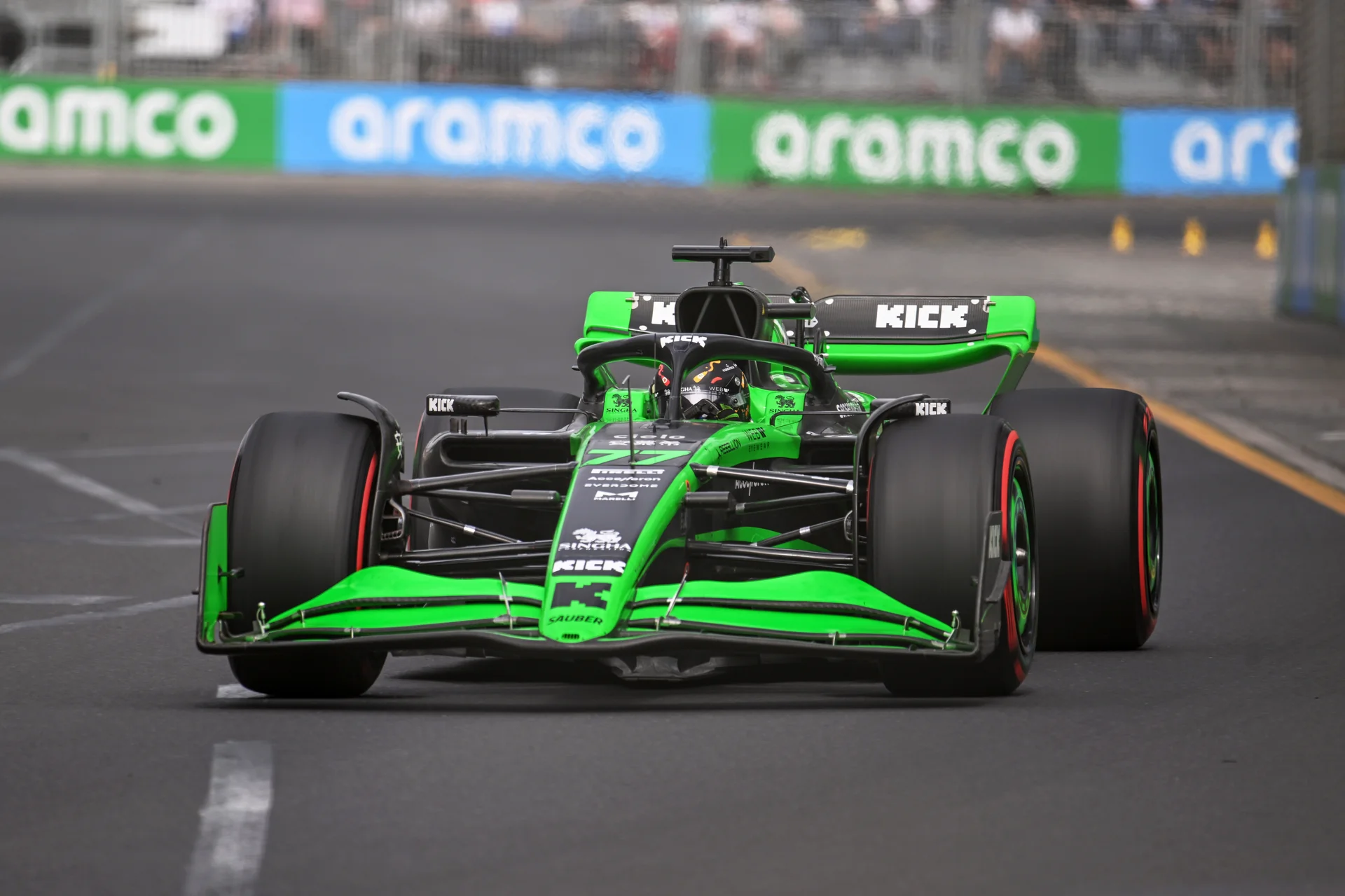 A green and black Formula 1 car speeding down the track at the Saudi Arabian Grand Prix, with grandstands and Aramco branding in the background.